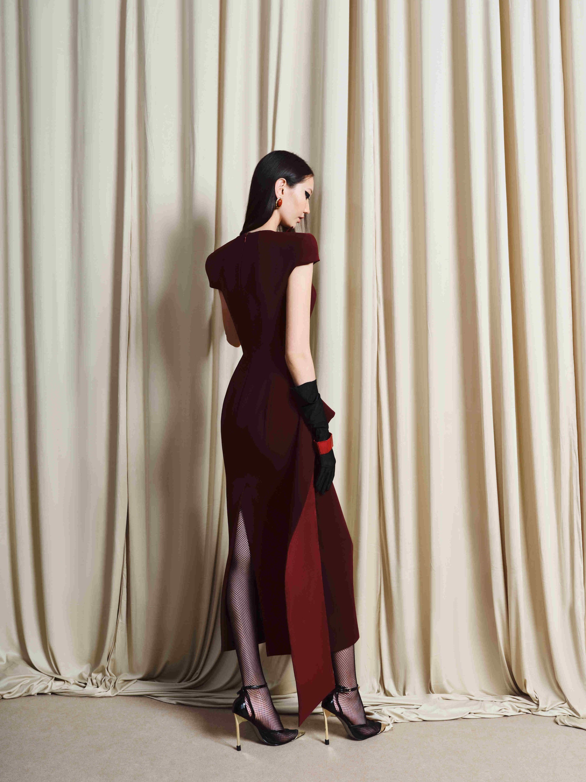 Woman in a burgundy dress standing in front of beige curtains