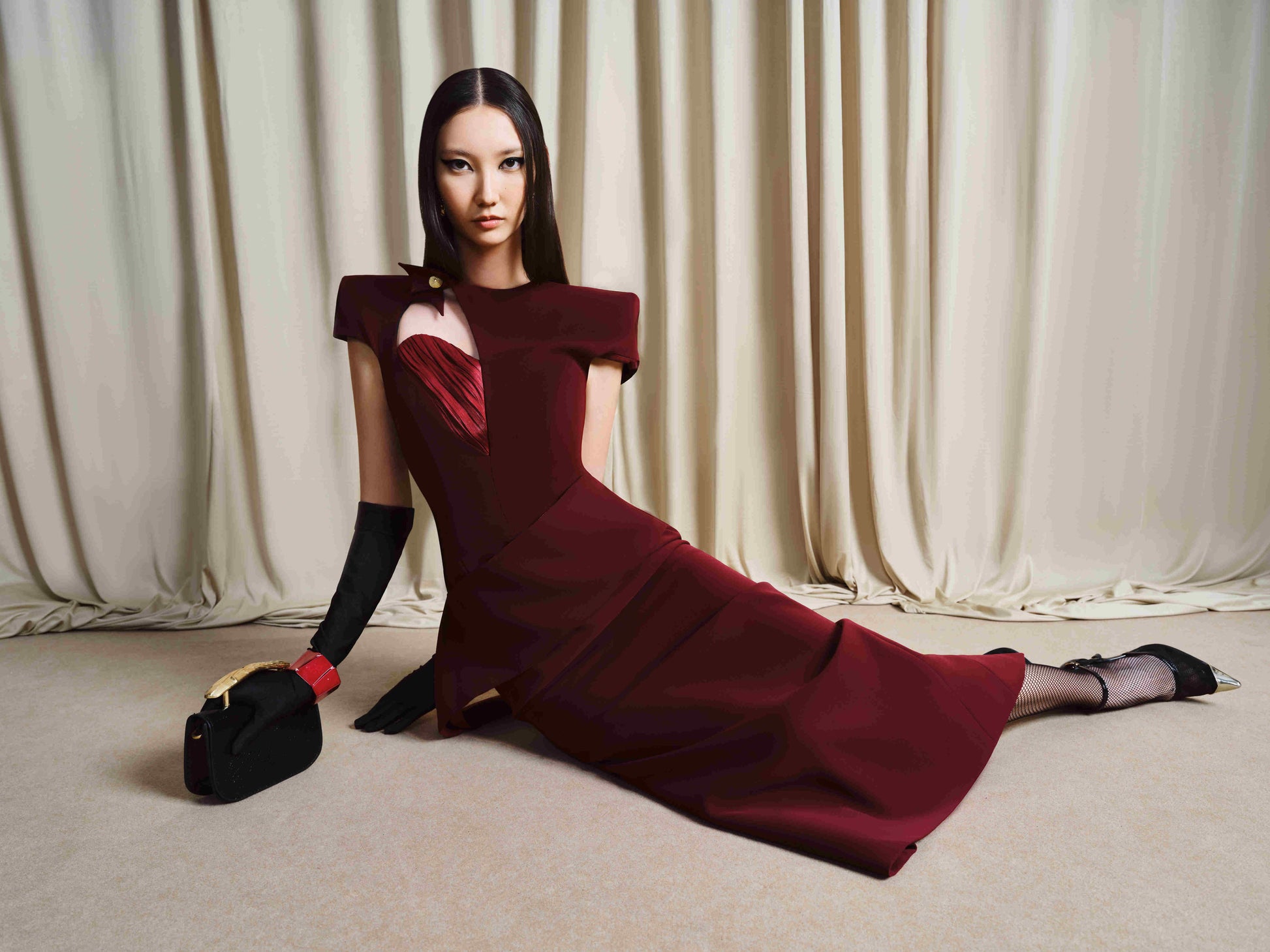 Woman in a burgundy dress sitting on the floor with a curtain background