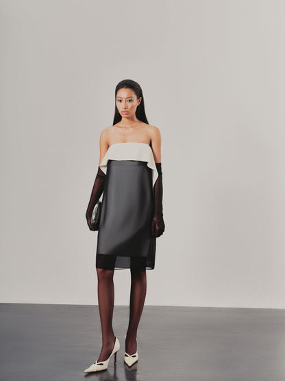 Model wearing a two-tone dress with a white top and black skirt on a plain background