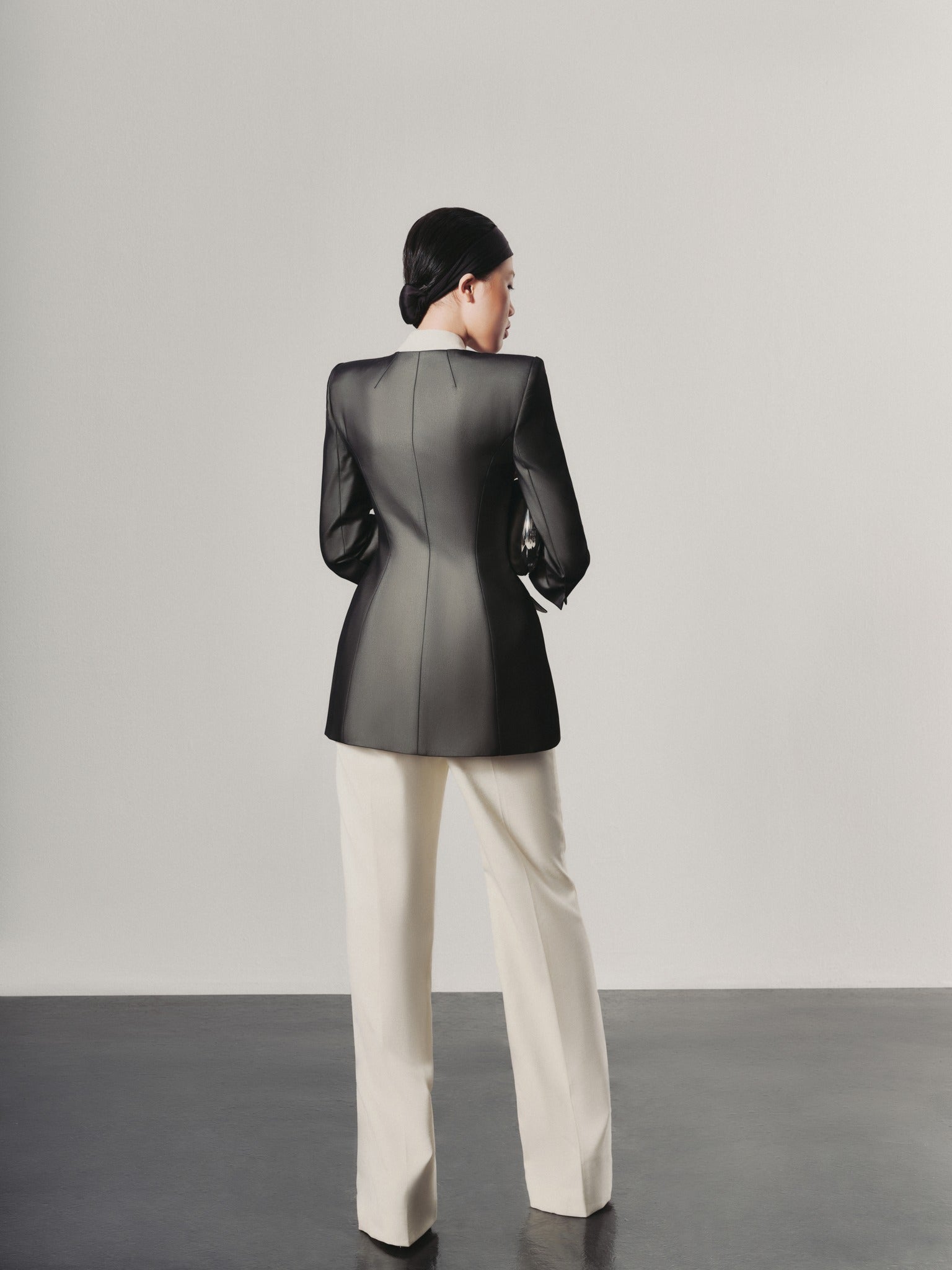 Person wearing a black jacket and white pants against a plain background