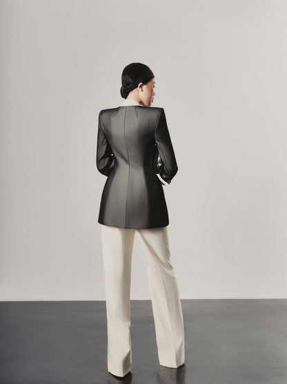 Person wearing a black jacket and white pants against a plain background