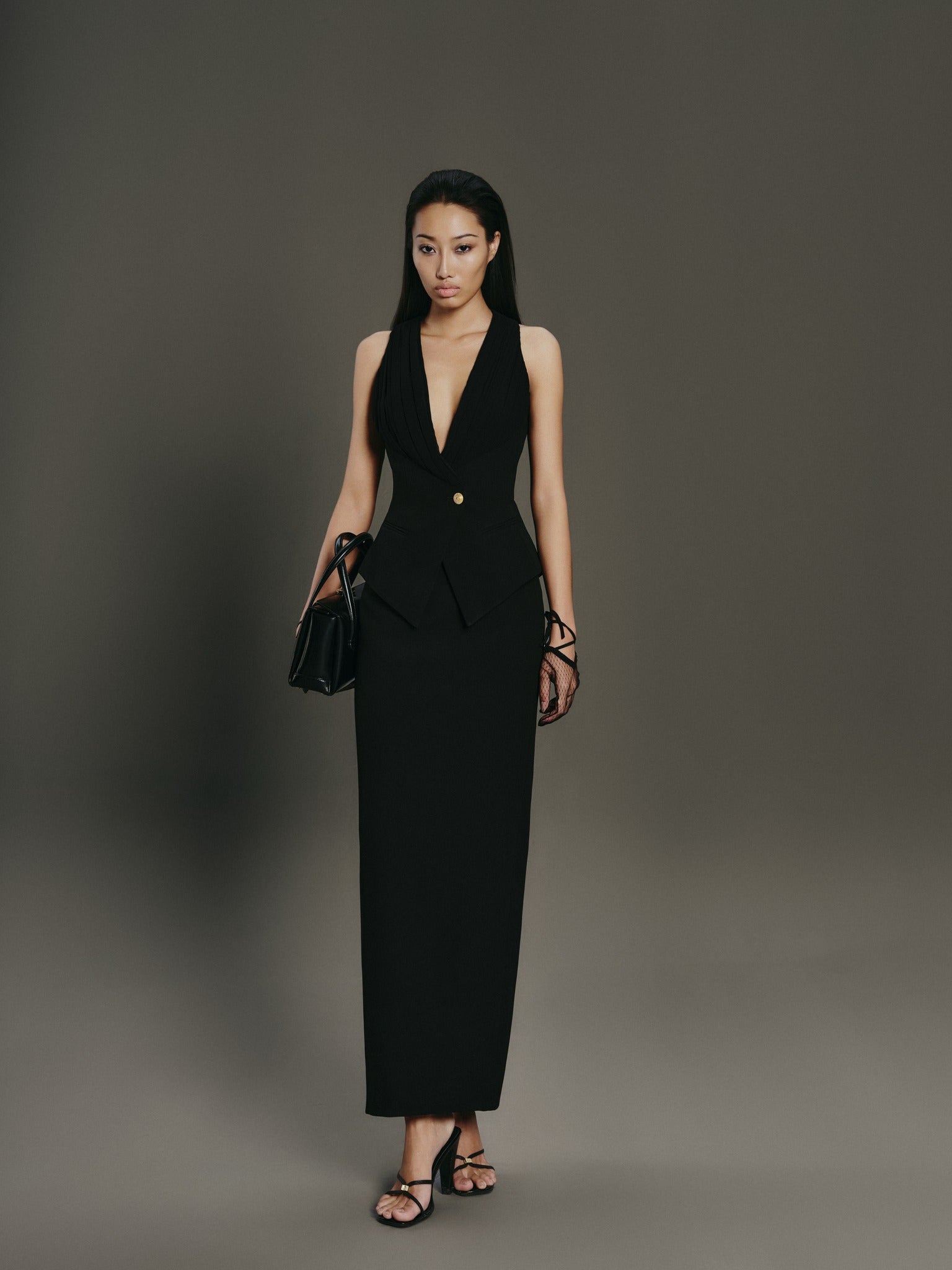 Woman wearing a black suit with a plunging neckline against a gray background