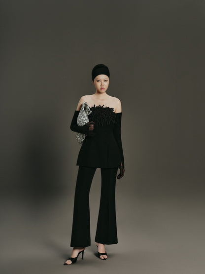 Woman in a black outfit holding a clutch against a gray background