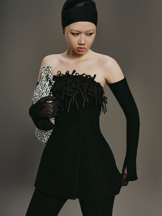 Model wearing a black outfit with fringe details against a gray background