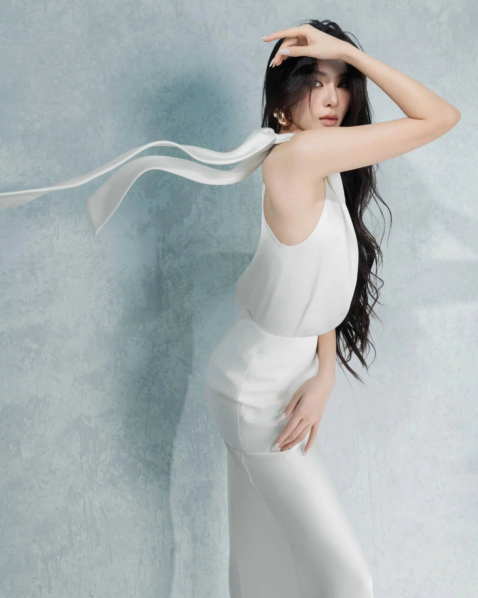 Woman in a white dress with a flowing ribbon against a light blue background