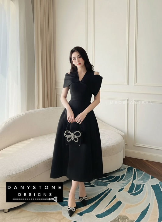 Woman in a black dress standing in a stylish room with a sofa and decorative rug.