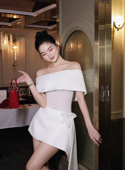 Woman in a white off-shoulder dress standing in an elegant interior setting.