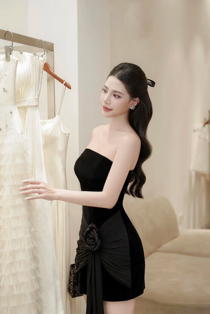 Woman in a black strapless dress standing in a room with white walls and furniture.