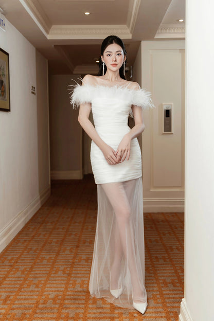 Woman in a white off-shoulder dress with feather details in a hallway.