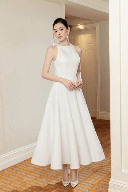 Woman in a white dress standing in an indoor setting with neutral walls.