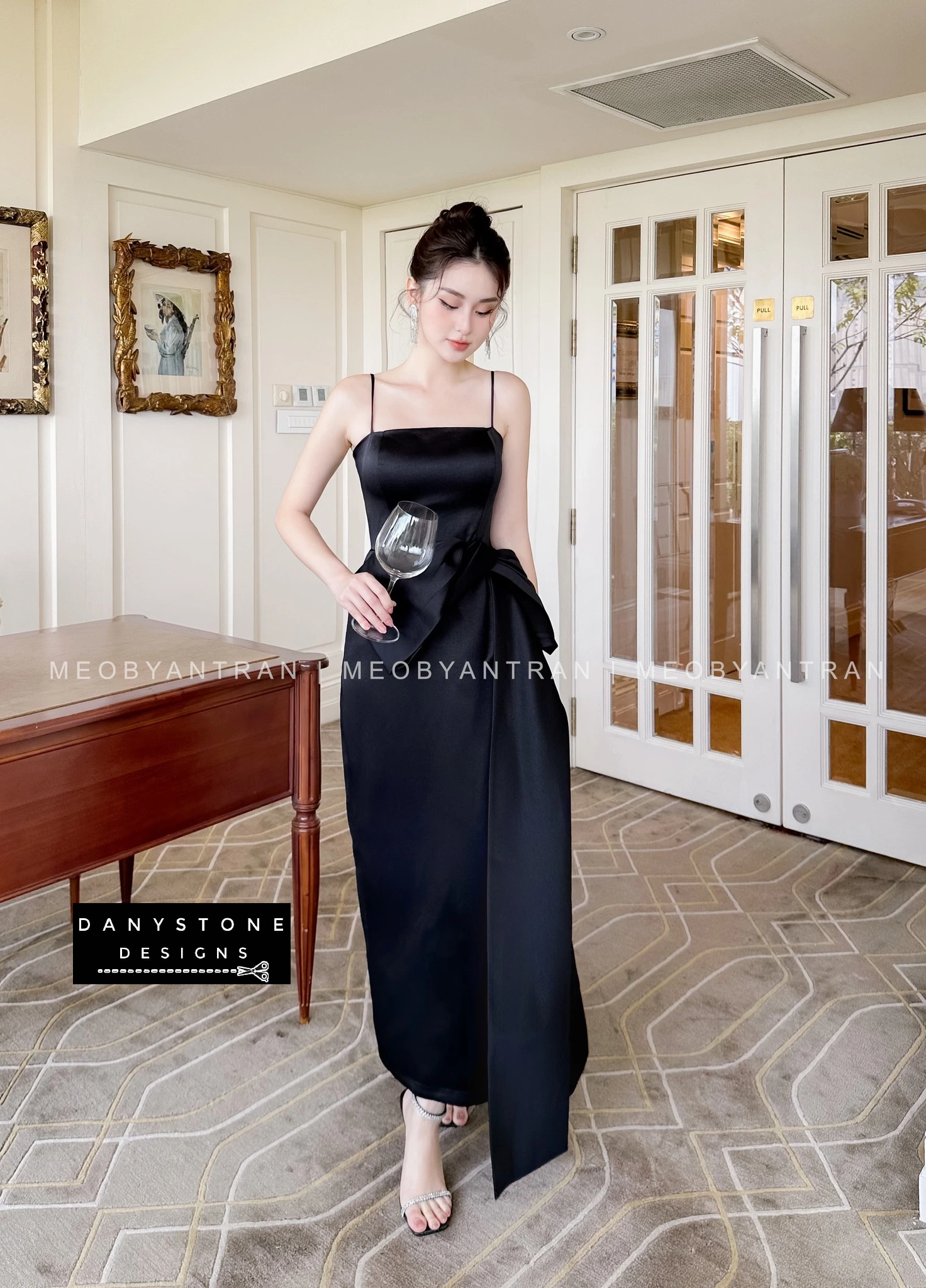 Model Posing in Black 2-Strap Dress with Bow Accent in Elegant Setting