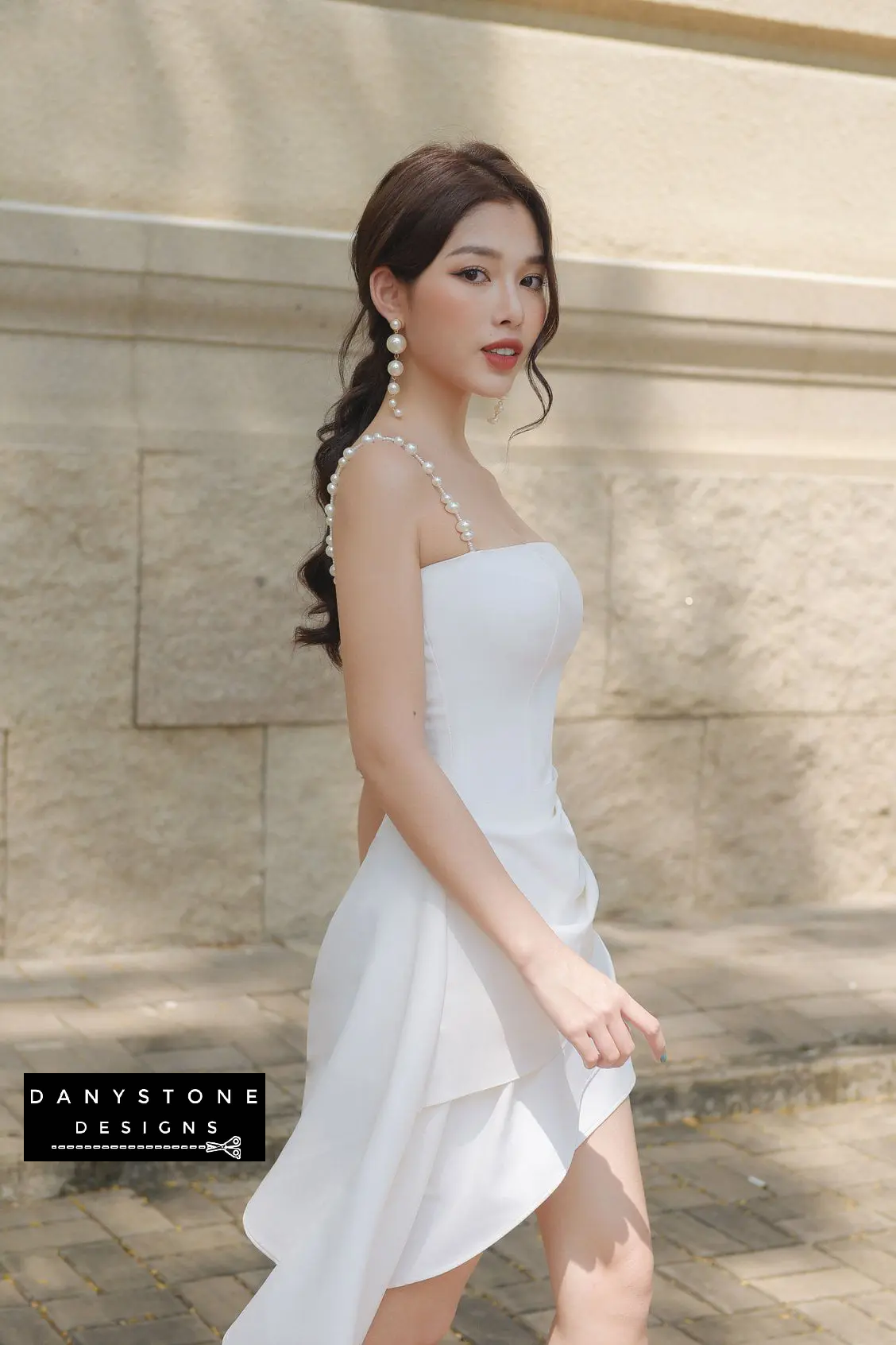 Woman in a white dress standing against a stone wall with 'Danystone Designs' branding.
