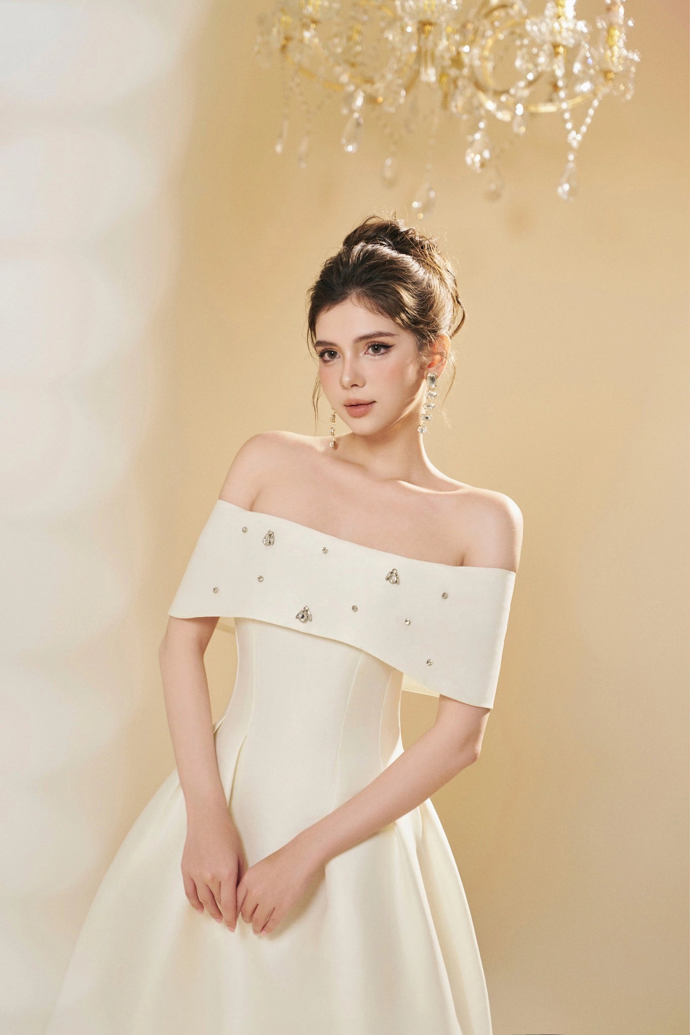 Woman wearing a white off-shoulder dress with embellishments against a soft yellow background.