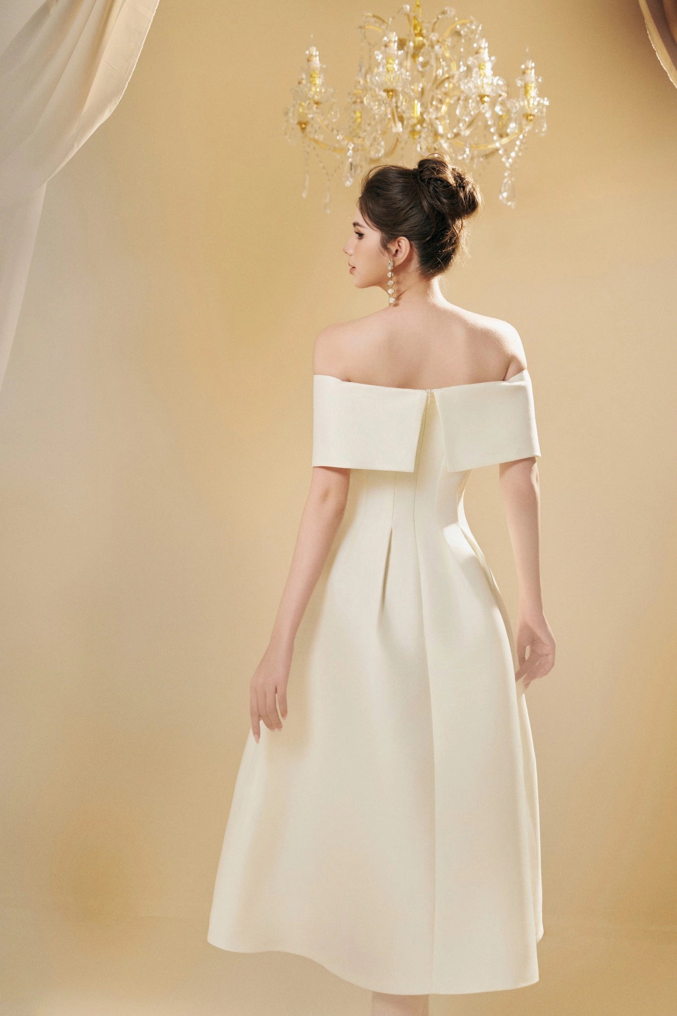 Woman wearing a white off-shoulder dress against a beige background