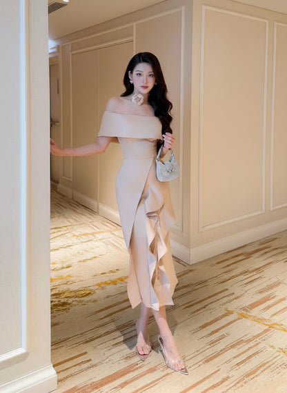 Woman in a beige off-shoulder dress standing in an elegant interior setting.