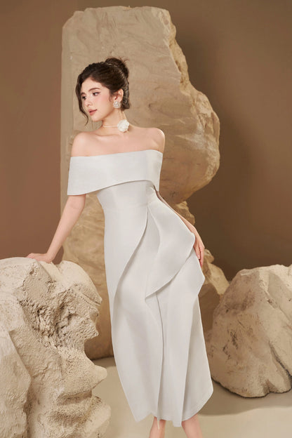 Woman in a light gray off-shoulder dress standing among large rocks.