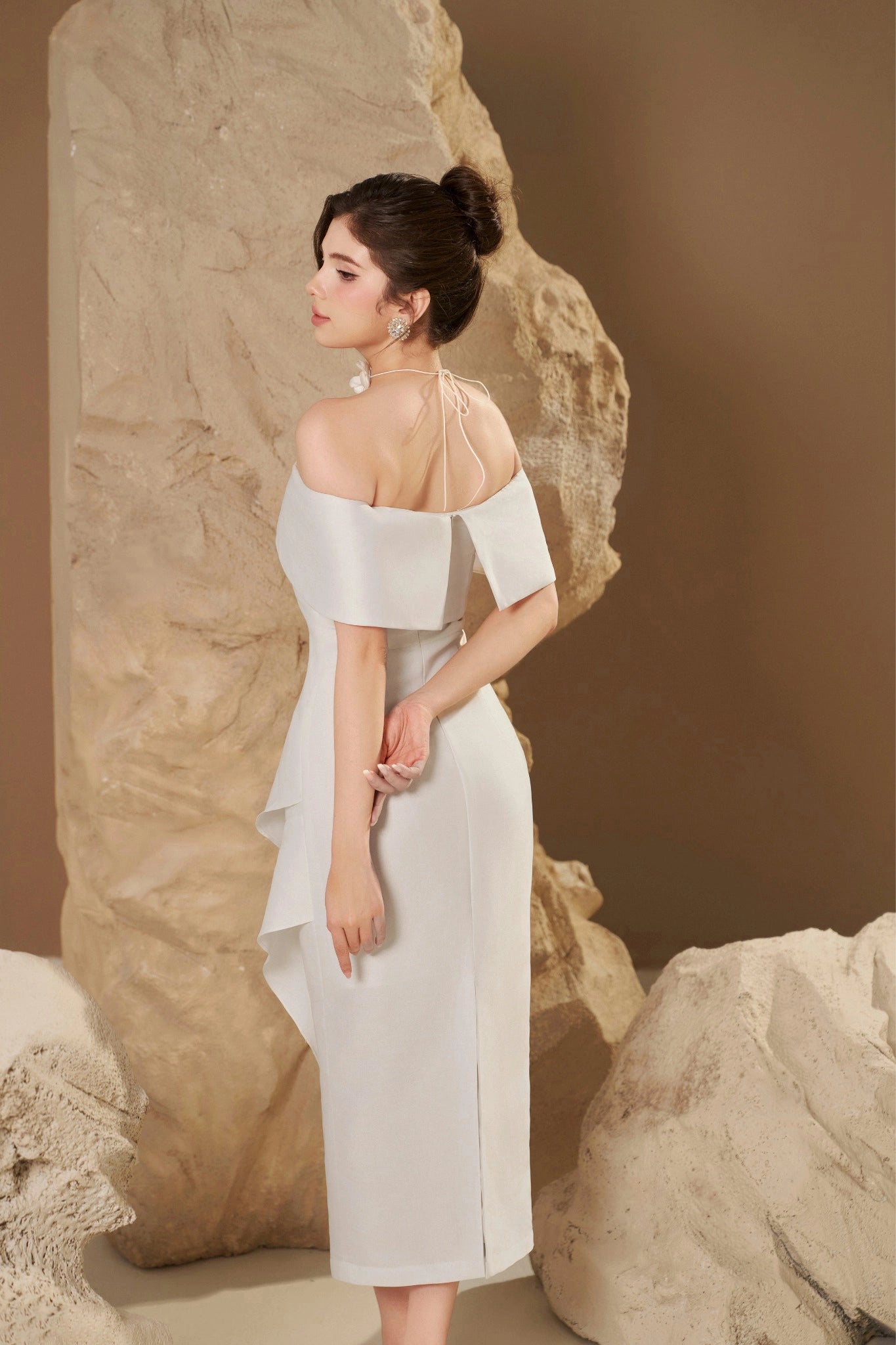 Woman in a white off-shoulder dress standing against a stone wall.