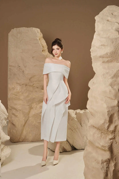 Woman in a light gray off-shoulder dress standing between large stone blocks.