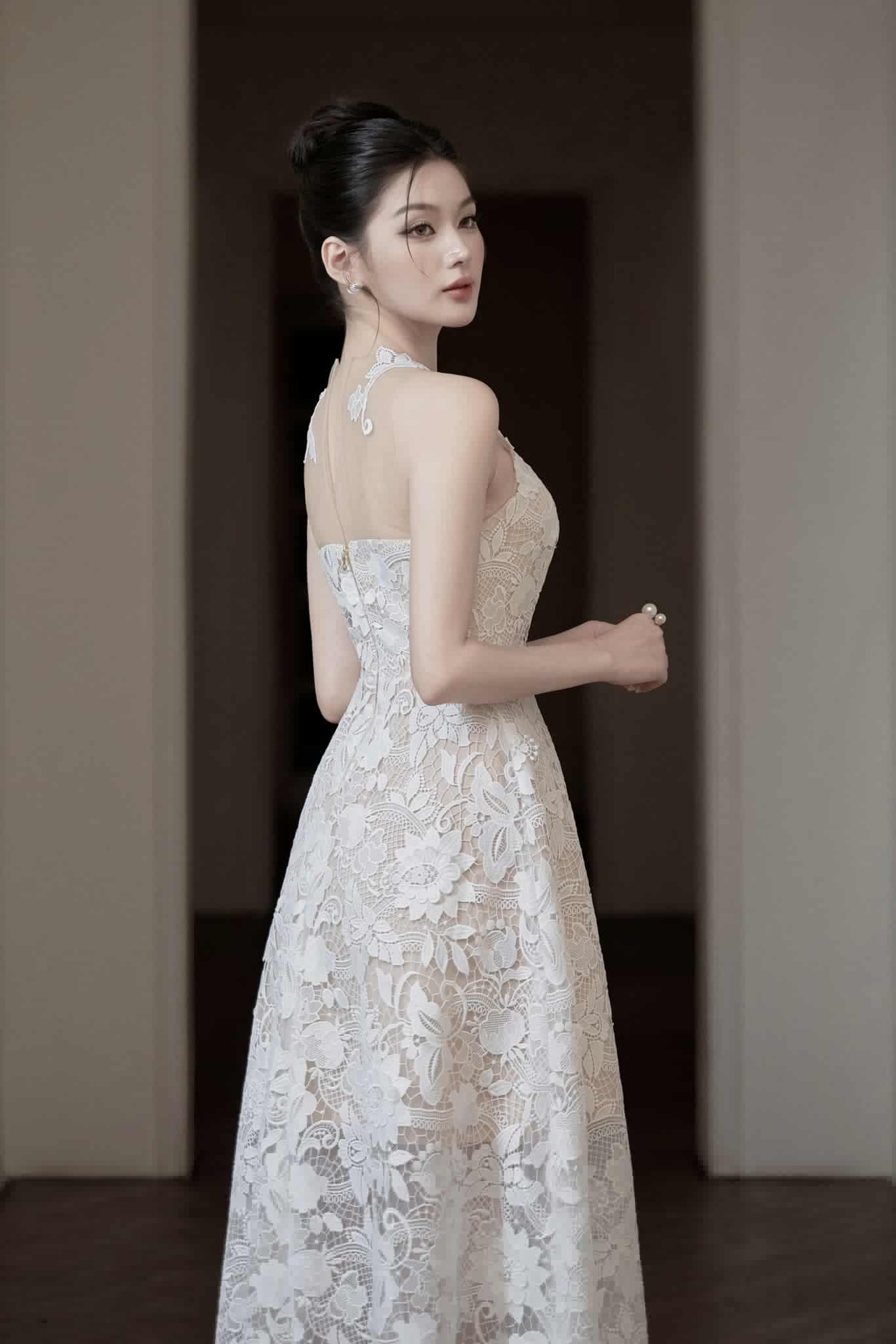 Woman in a white lace dress standing against a neutral background