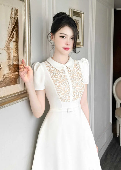 Woman in a white dress with lace details standing in an elegant room.