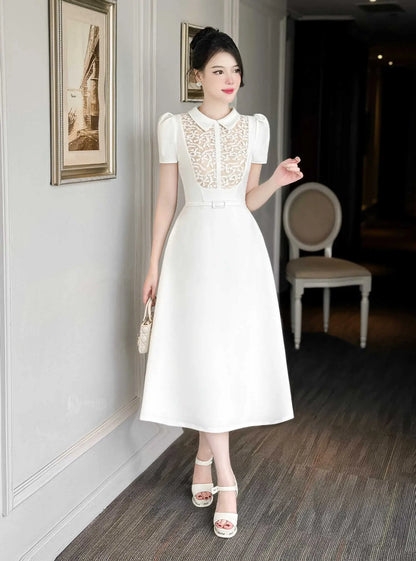Woman in a white dress standing in an indoor setting with framed pictures on the wall.