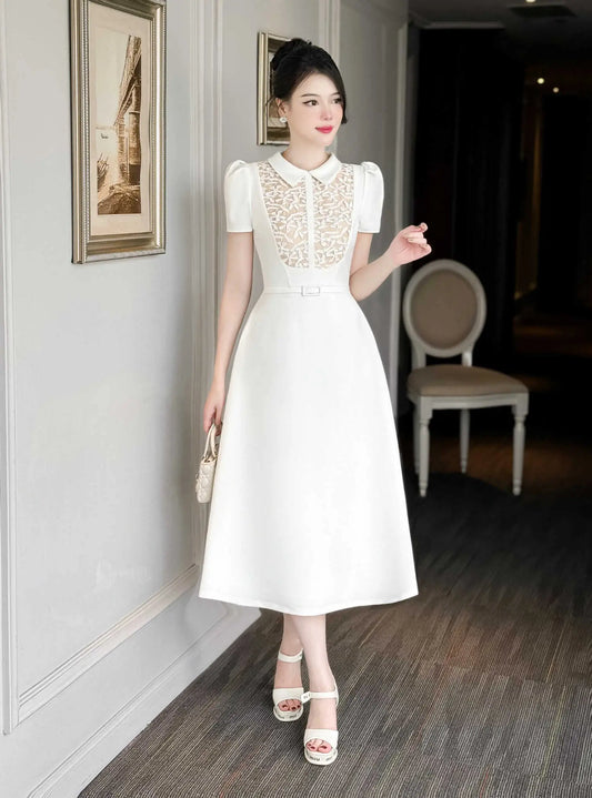 Woman in a white dress standing in an indoor setting with framed pictures on the wall.