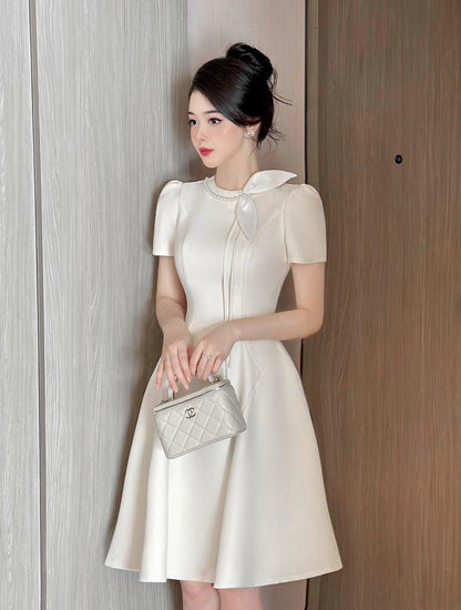 Woman in a white dress holding a silver handbag against a wooden door.