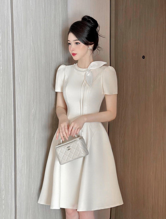 Woman in a white dress holding a silver handbag against a wooden door.