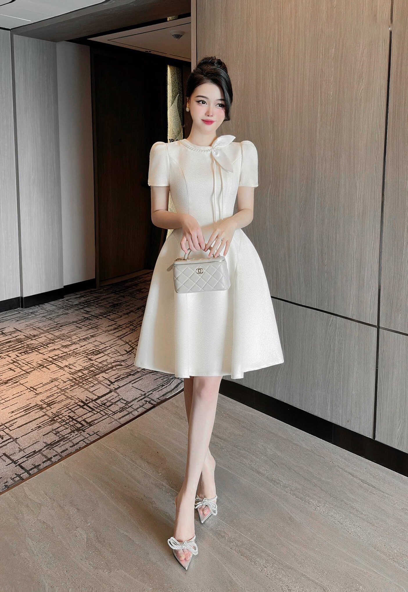 Woman in a white dress holding a handbag in an indoor setting