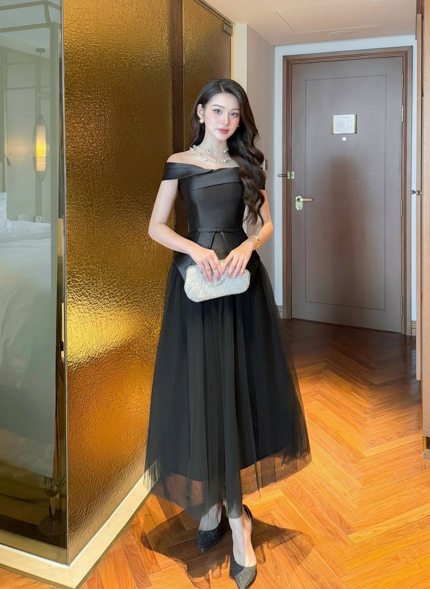 Woman in a black off-shoulder dress standing in a room with wooden flooring and gold walls.