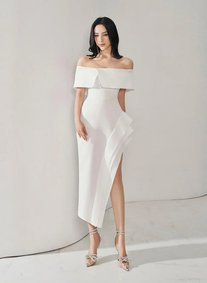 Woman wearing a white off-shoulder dress with a high slit on a plain background