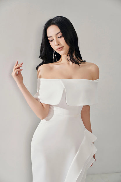 Woman wearing a white off-shoulder dress against a plain background