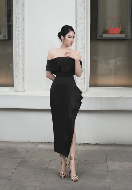 Woman in a black off-shoulder dress standing against a white wall.