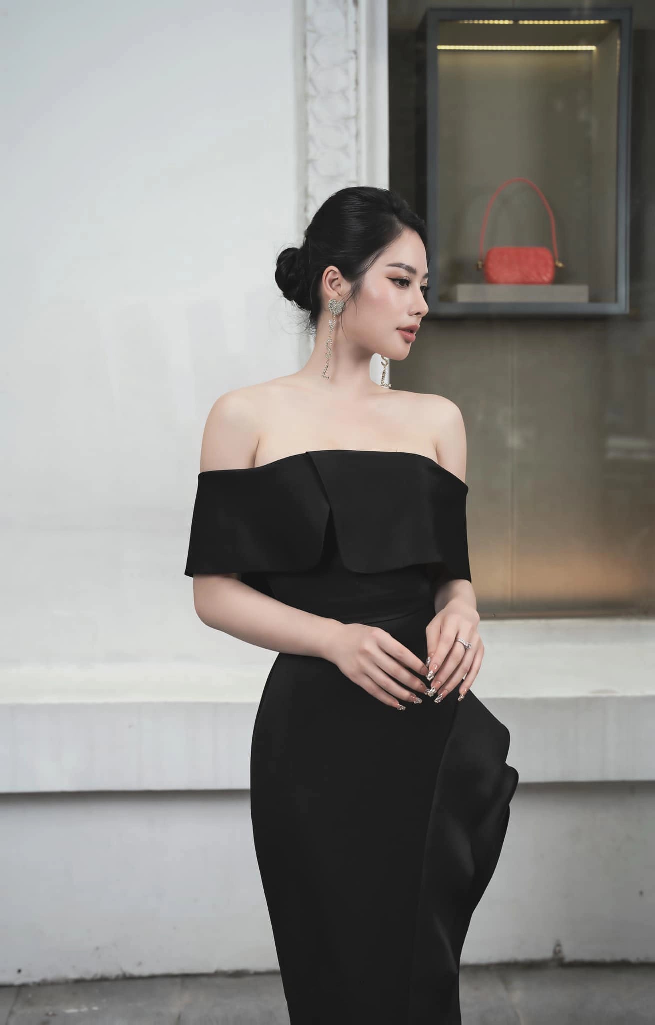 Woman in a black off-shoulder dress standing against a plain background
