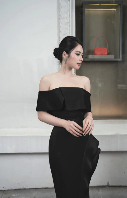Woman in a black off-shoulder dress standing against a plain background