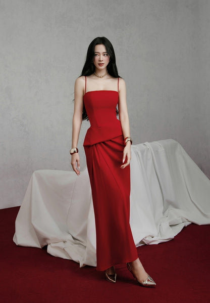 Woman in a red dress standing against a gray background with draped fabric.