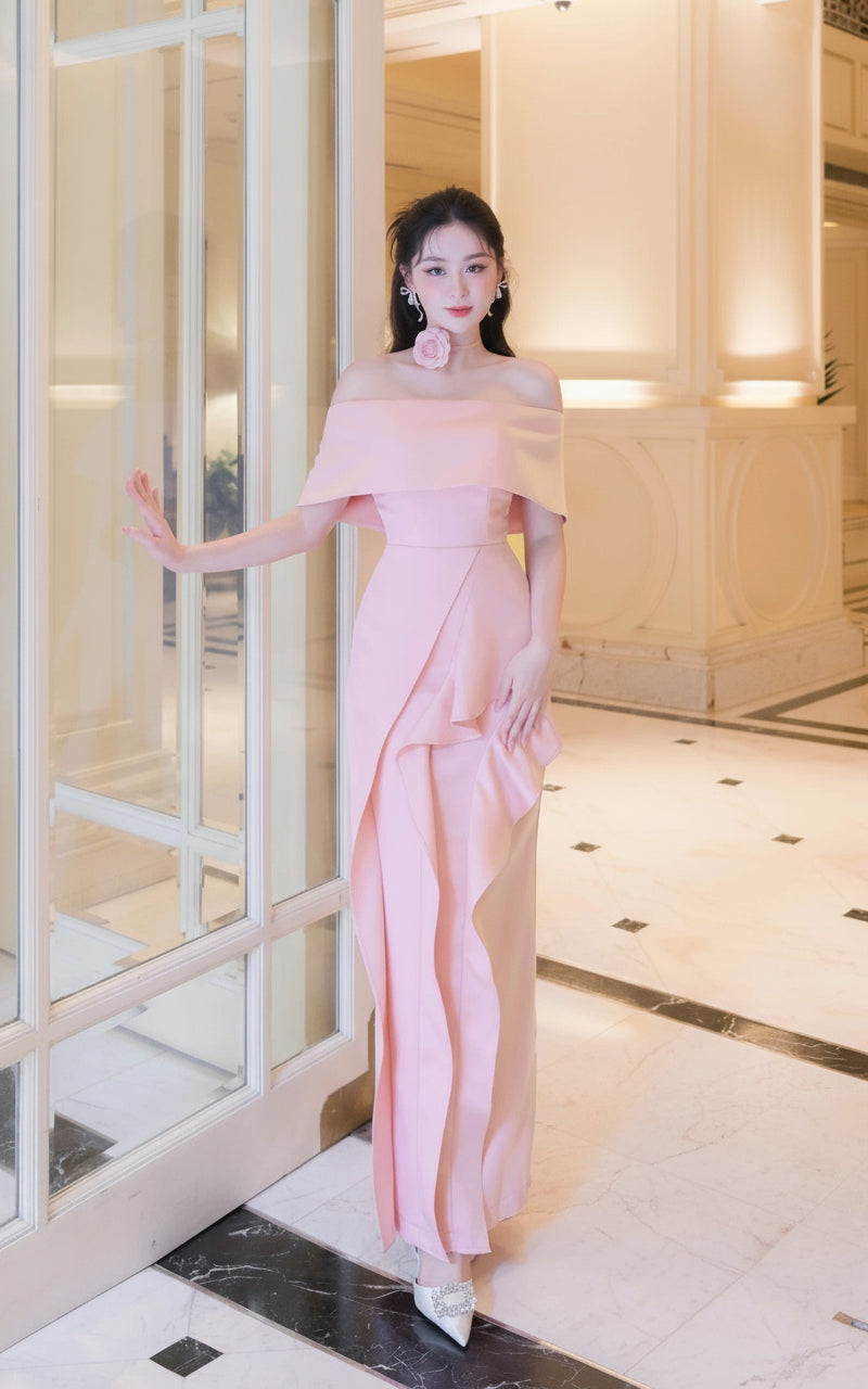 Woman in a pink off-shoulder dress standing in a luxurious interior setting.