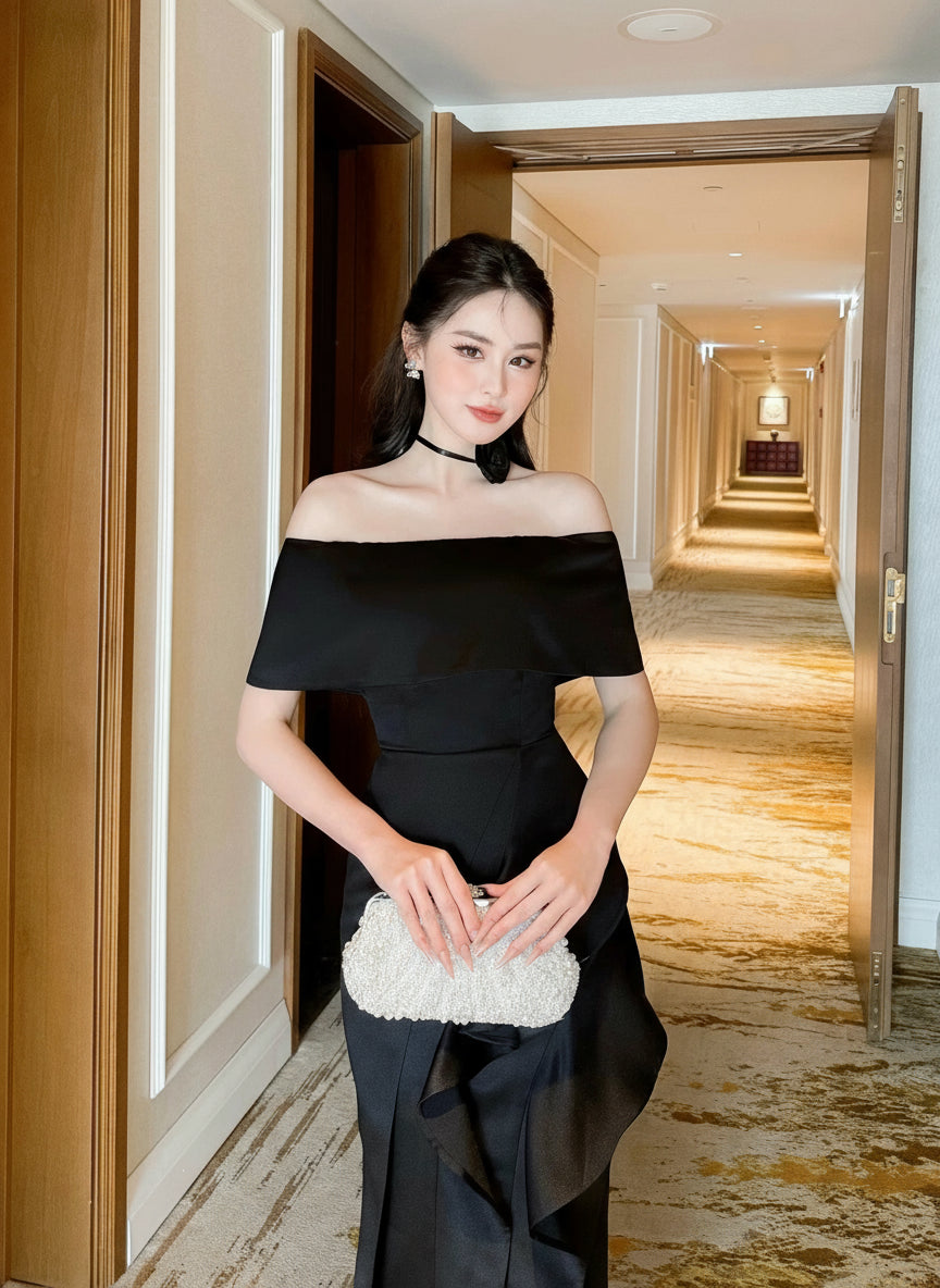 Woman in a black off-shoulder dress holding a white clutch in a hallway.