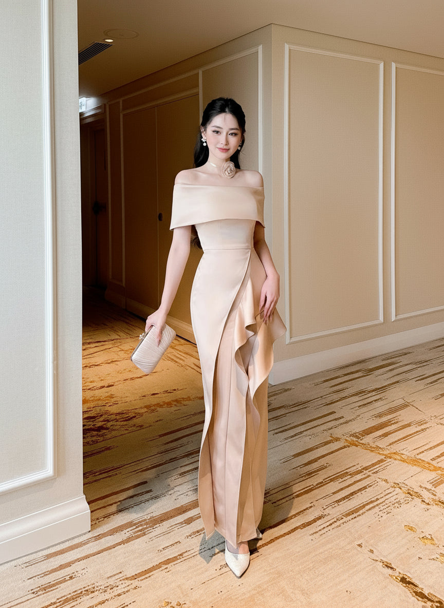 Woman in a beige off-shoulder gown standing in an elegant interior setting.
