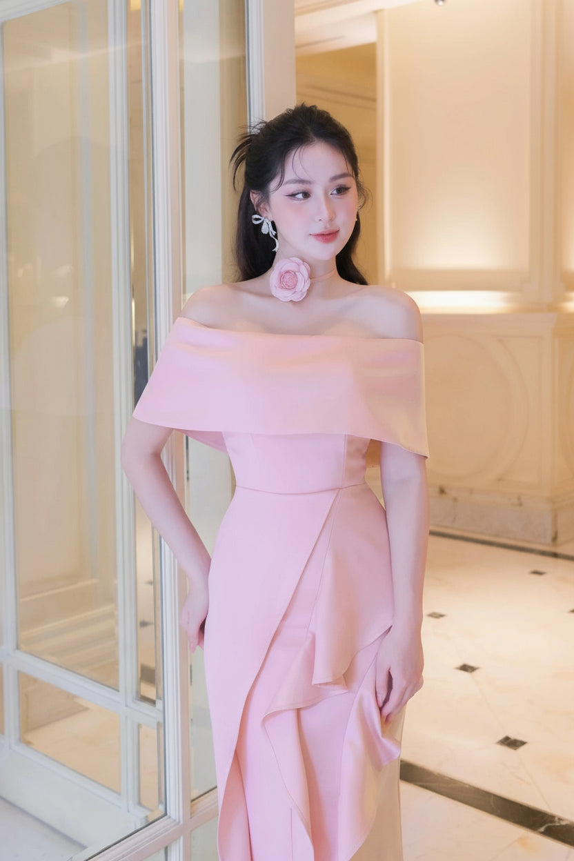 Woman in a pink off-shoulder dress standing indoors with a blurred background