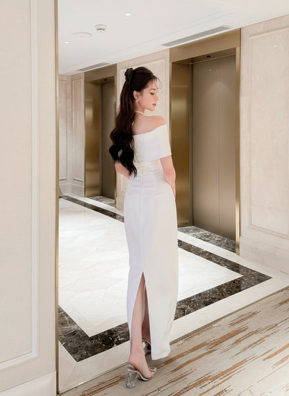 Woman in a white off-shoulder dress standing in a modern elevator lobby.