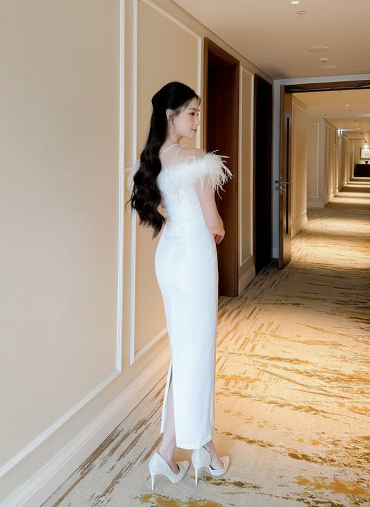 Woman in a white evening gown with feather details standing in a hotel hallway.
