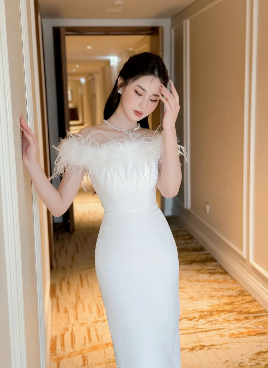 Woman in a white evening gown with feathered shoulders standing in a hallway.