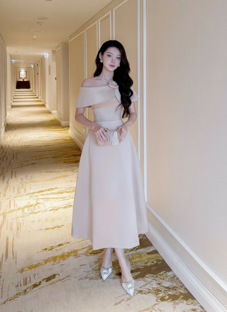 Woman in a beige off-shoulder dress standing in a hotel hallway.