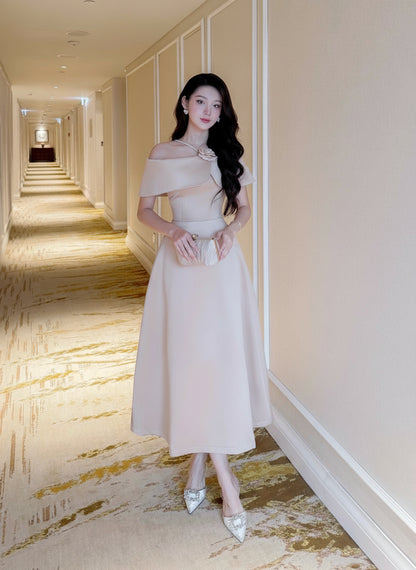 Woman in a beige off-shoulder dress standing in a hotel hallway.