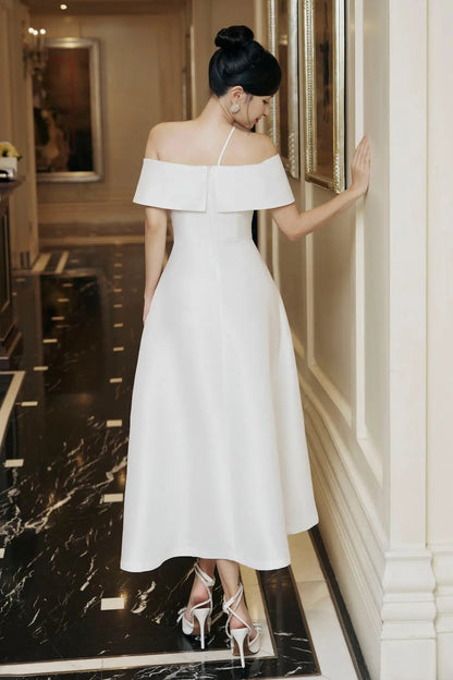 Woman in a white off-shoulder dress standing in a hallway.