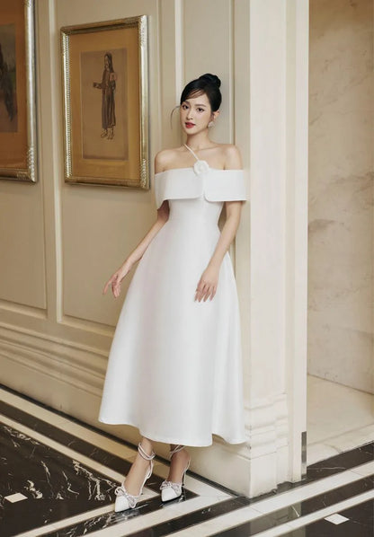 Woman in a white off-shoulder dress standing in an elegant interior setting.