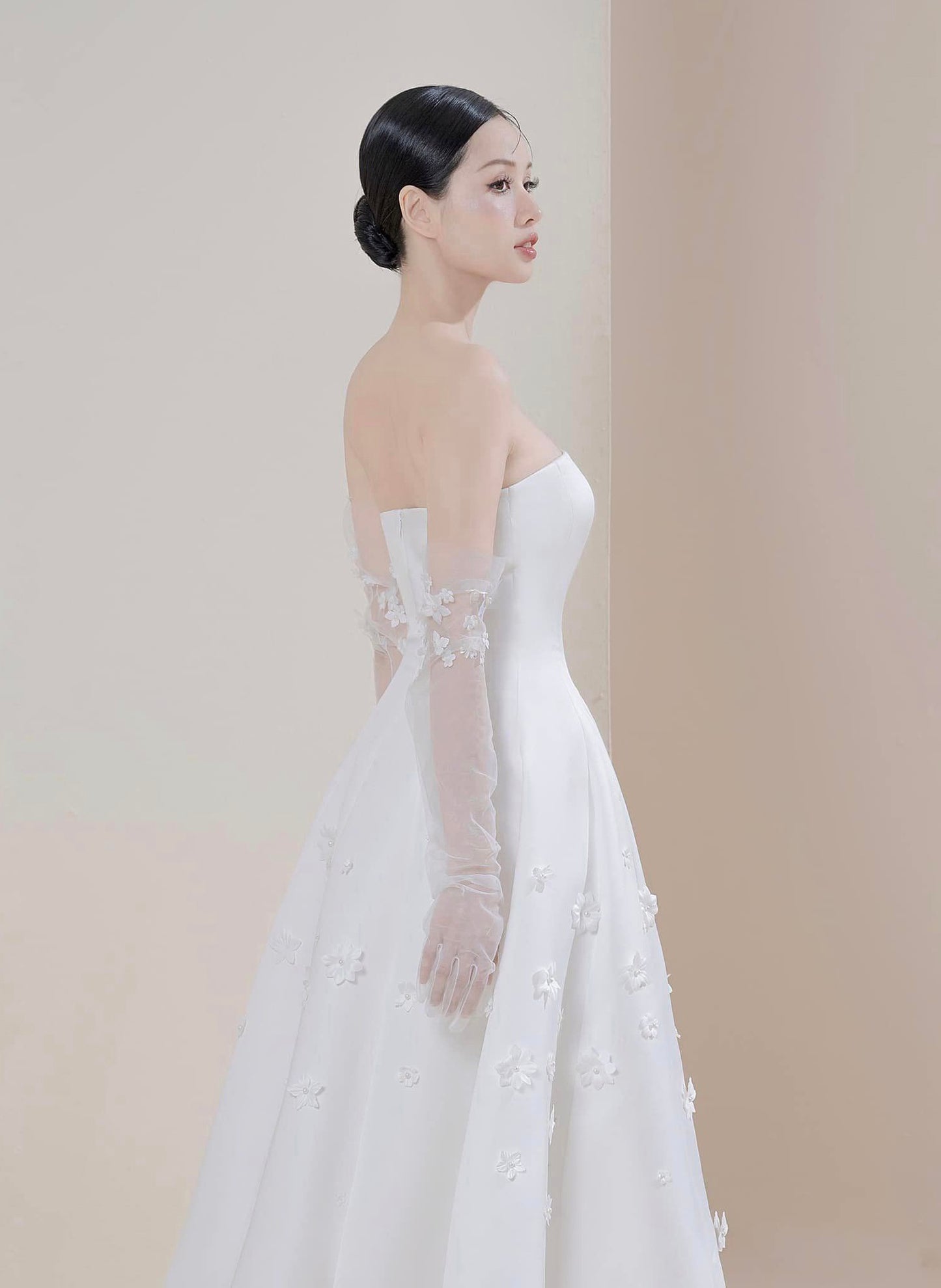 Woman wearing a white wedding dress with floral details on a plain background