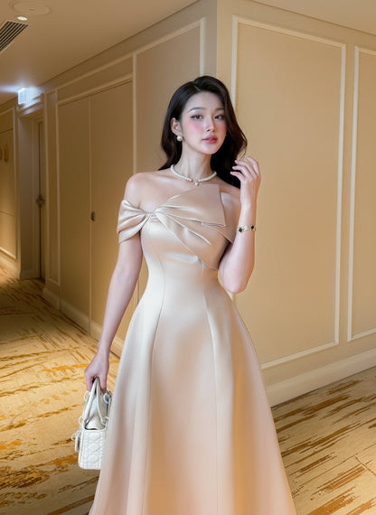 Woman in a beige off-shoulder dress standing in an elegant interior setting.