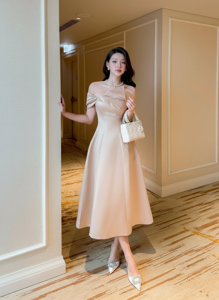 Woman in a beige dress standing in a room with wooden flooring and white walls.